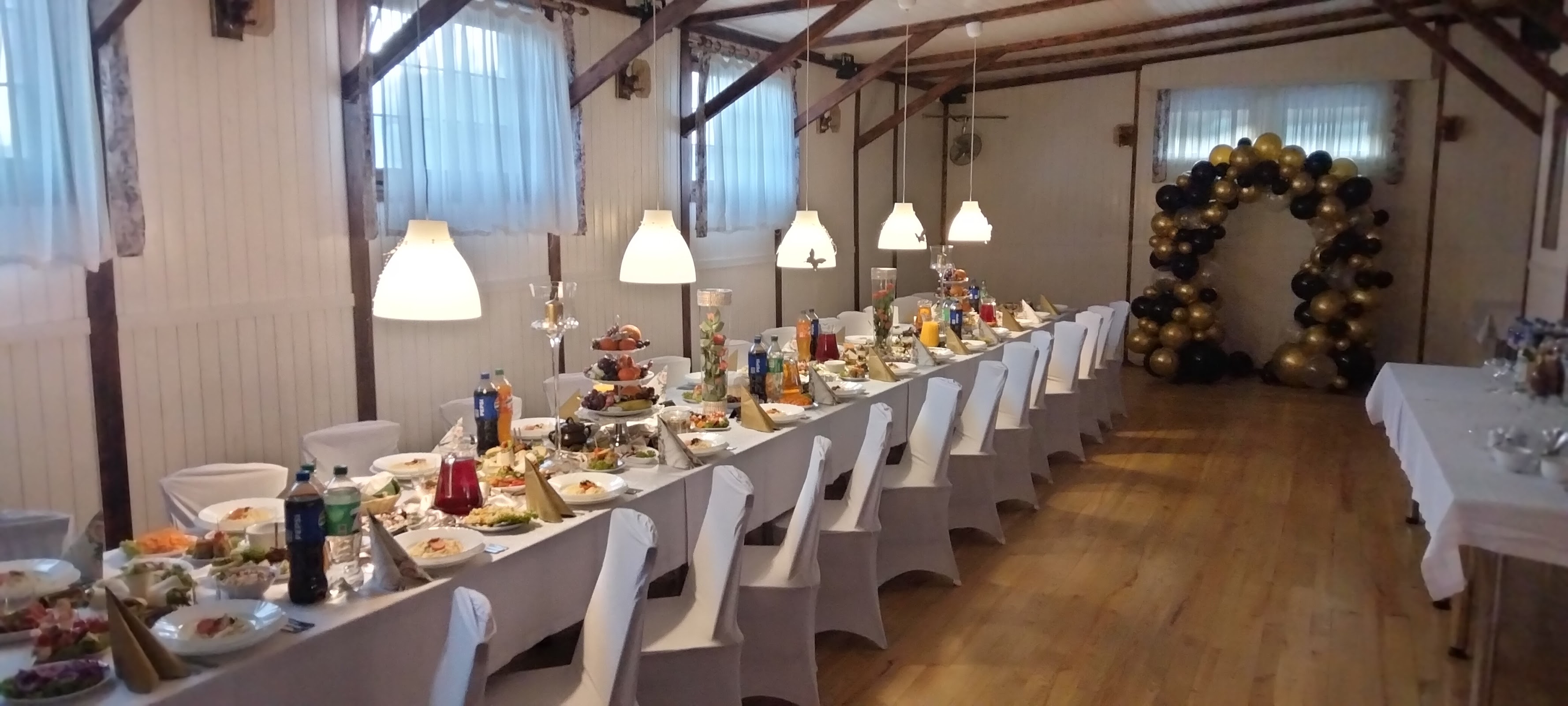 Sala biesiadna od wejścia - długie stoły, drewniane belki, łuk balonów w głębi