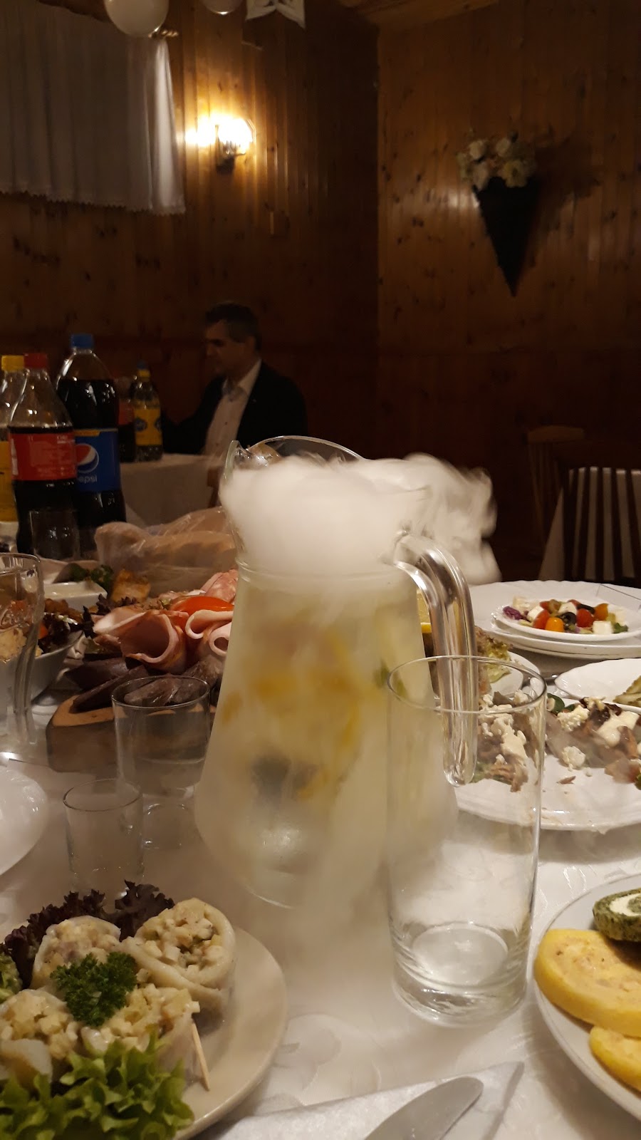Suchy lód paruje z dzbanka oranżady - efektowny moment podczas przyjęcia w Góreckiej Chacie, na stole półmisek wędlin i sałatka grecka